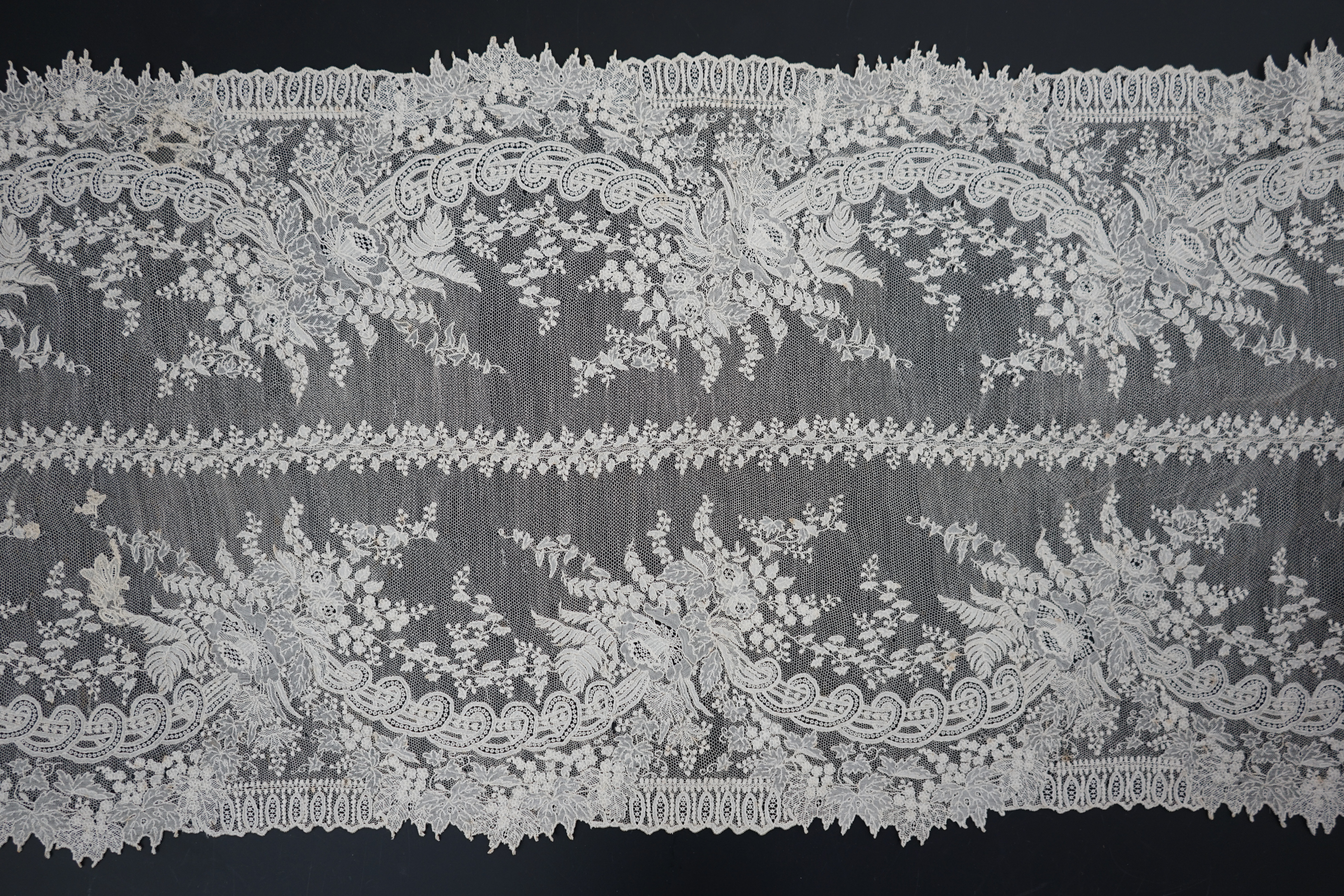 A 19th century Brussels Point de gaze needle lace stole 228cm long x 37cm wide, made from two lengths of the same patterned lace, invisibly joined along the centre of the stole, the raw end edges carefully finished with